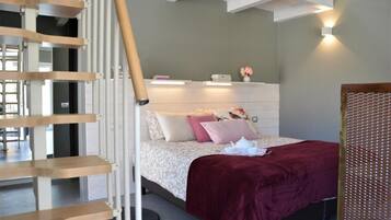 Un dormitorio con cama, una escalera de madera, una mesita de noche y una lámpara fijada a la pared.