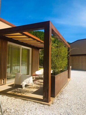 A modern outdoor patio with a pergola, seating area, and a planter with greenery.