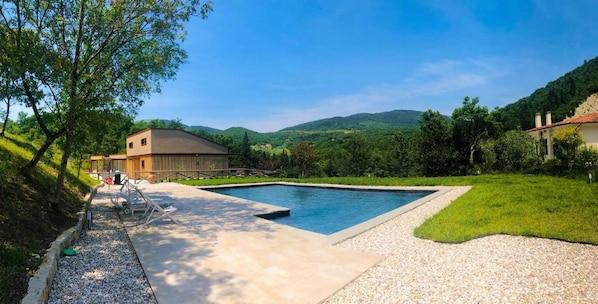A swimming pool with a surrounding deck, a wooden cabin, and a mountainous landscape in the background.