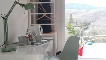 A modern room with a desk, a green chair, a white shelf unit, and a view of a mountainous landscape.