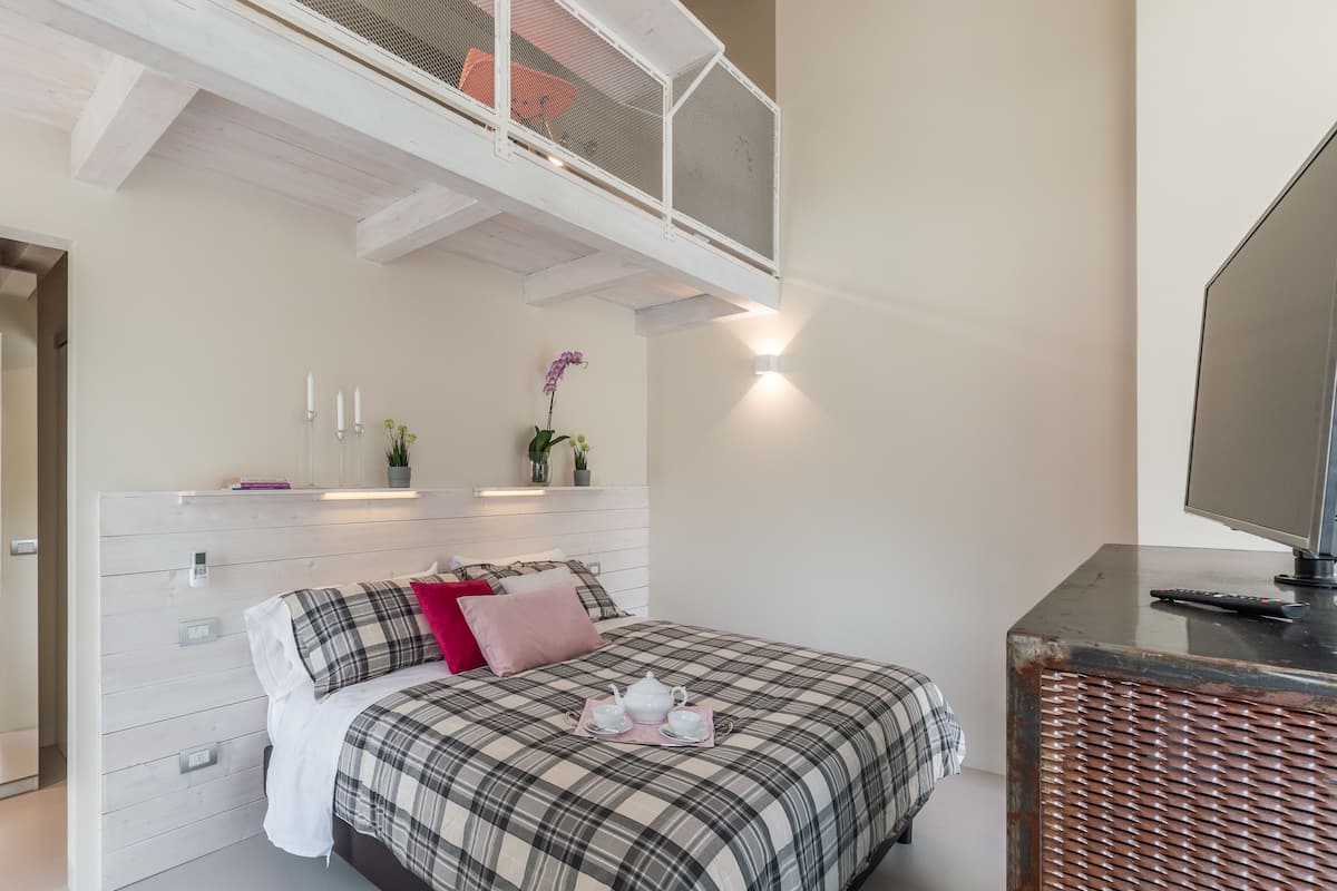 A bedroom with a bed, bedside tables, a TV, and a balcony with a railing.