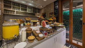 A breakfast bar with various food and drink options, including a fruit bowl, a juice dispenser, and a selection of bowls and plates. - Samann Host (Hulhumalé)