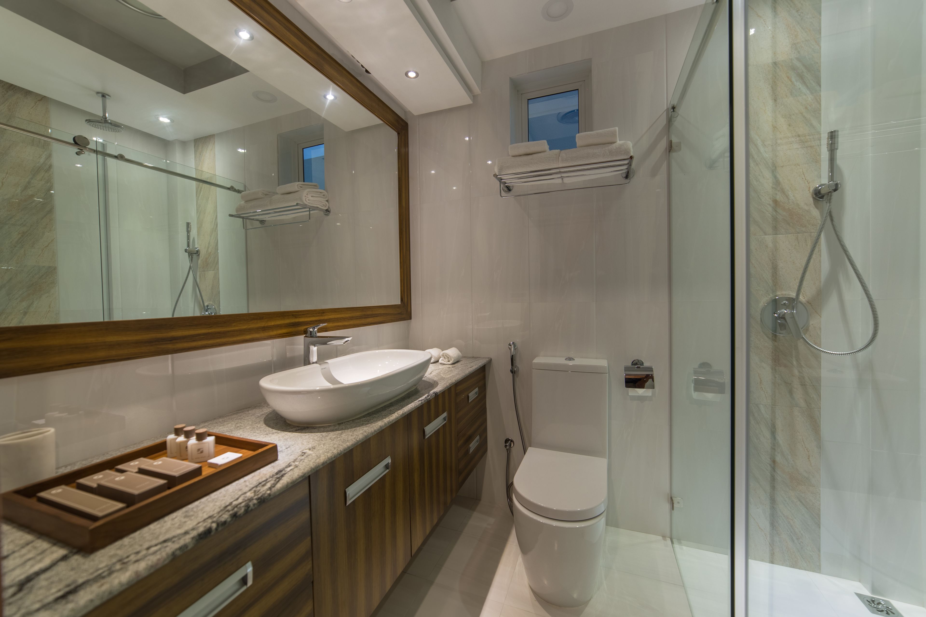 A modern bathroom with a glass-enclosed shower, a large mirror, a white sink, and wooden cabinets.