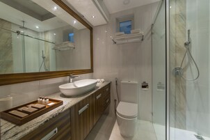 Un baño moderno con ducha de vidrio, un espejo grande, un lavamanos blanco y armarios de madera.