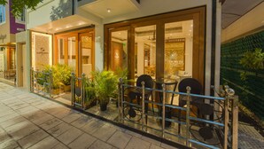 A well-lit outdoor seating area with a glass railing, potted plants, and a view of the interior of a building. - Samann Host (Hulhumalé)