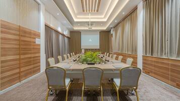 A conference room with a long table, multiple chairs, a projector screen, and a plant centerpiece.