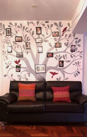 Relax in this stylish living room with a comfortable sofa, artistic tree design, and family photographs.