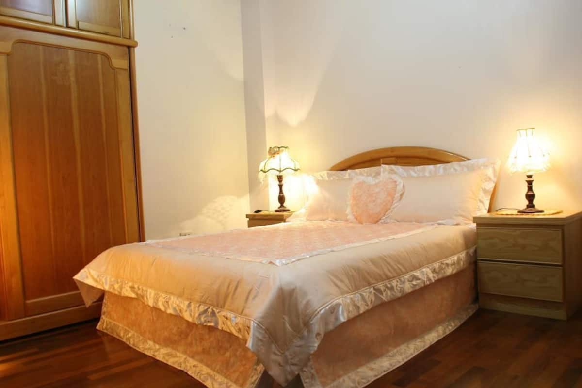 A neatly made bed with a wooden headboard, two bedside lamps, and a wooden nightstand with drawers.