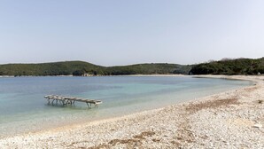 Ein Strand mit klarem Wasser, einer Holzsteganlage und einem Kiesstrand.
