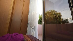 Ein Zimmer mit einem Bett, einem Holzschrank und einer Glastür, die auf einen Balkon mit Pflanzen führt.
