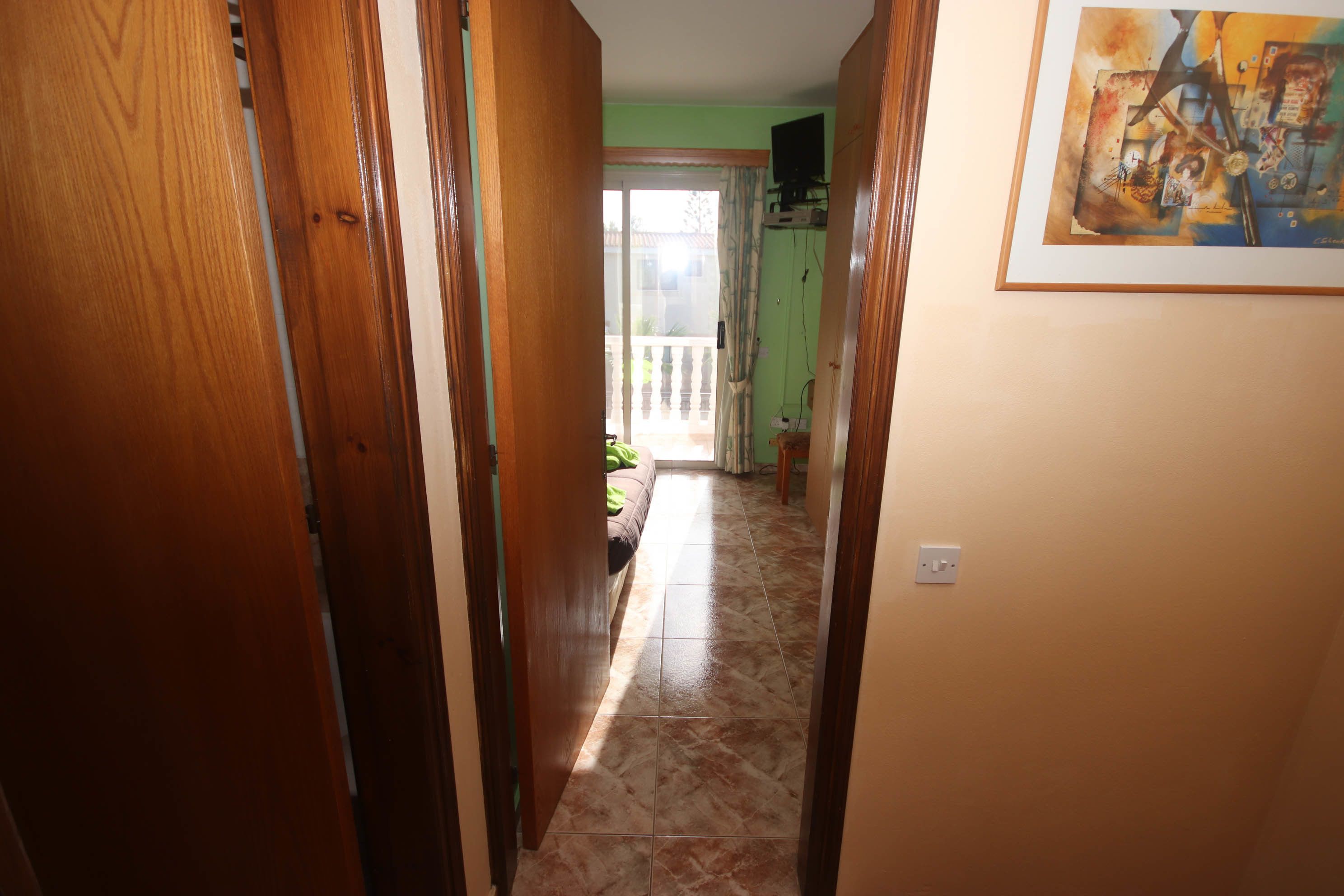 A hallway with wooden doors, a tiled floor, and a painting on the wall.