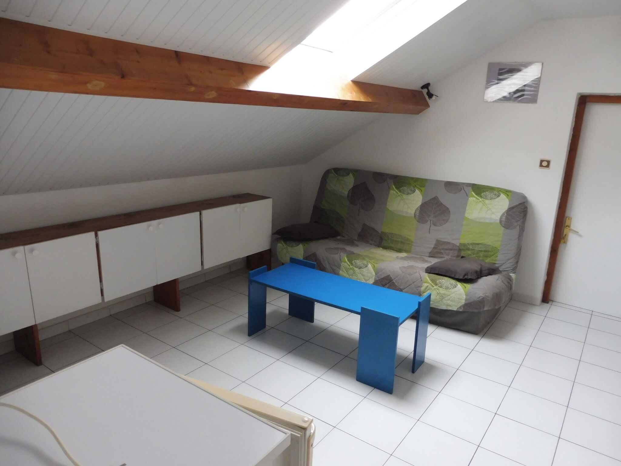 A room with a sloped ceiling, a sofa with a leaf-patterned cover, a blue table, and white cabinets.