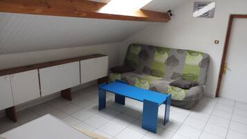 A room with a sloped ceiling, a sofa with a leaf-patterned cover, a blue table, and white cabinets.
