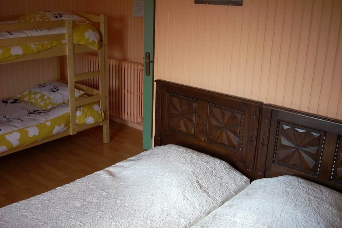 Quarto com beliches, cabeceira de madeira, radiador e uma pequena imagem na parede.