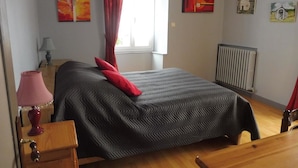 Une chambre à coucher comprenant un lit, une table de chevet, une lampe, une fenêtre avec des rideaux et des œuvres d’art murales.