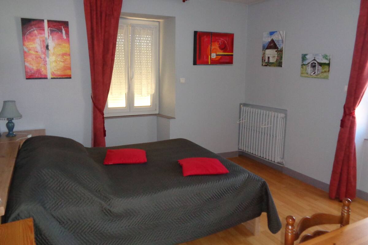 Quarto com cama, janela com cortinas, radiador e obras de arte nas paredes.