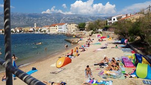Una playa con gente tomando el sol y nadando, tiendas de campaña y sillas de playa.