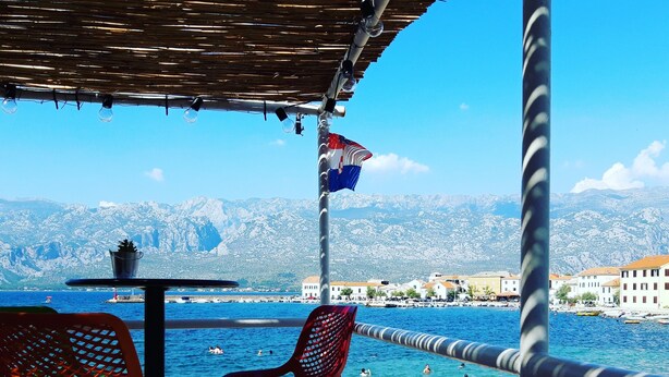 Una terraza frente al mar con mesas al aire libre, vistas al océano y una bandera.