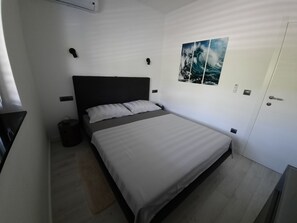 Een moderne slaapkamer met een groot bed, een nachtkastje, een wandlamp, een schilderij en een deur met een deurklink.
