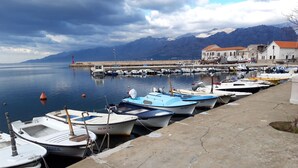 Un puerto deportivo con varias embarcaciones pequeñas amarradas a la orilla, un muelle que se adentra en el agua y montañas al fondo.