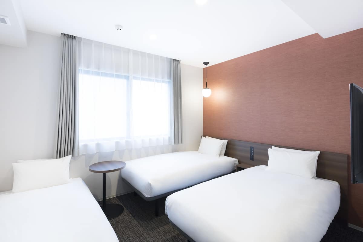 A hotel room with two beds, a small round table, and a large window with curtains.