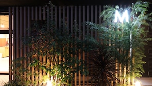 A building facade with vertical wooden slats and a prominent illuminated 'M' sign. - M’s Hotel Sanjo Omiya (Kyoto)