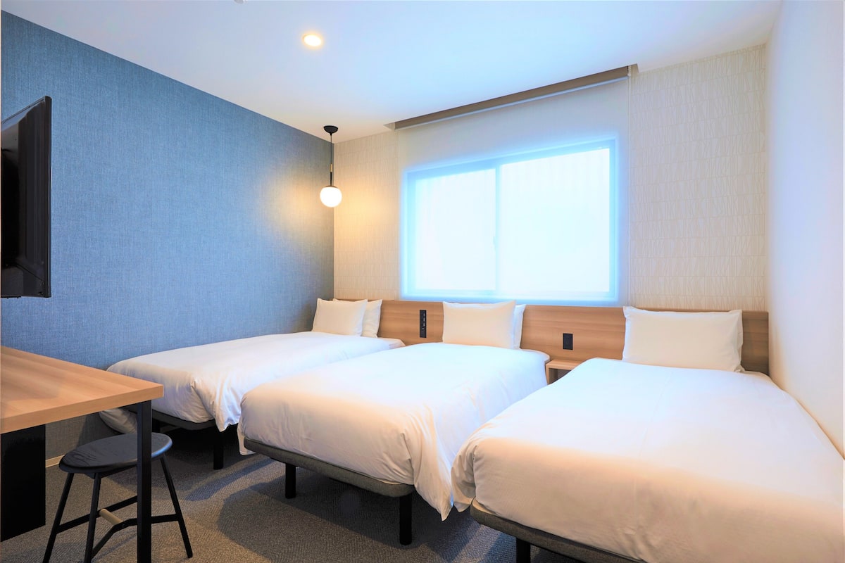 A hotel room with two single beds, a desk, and a chair.