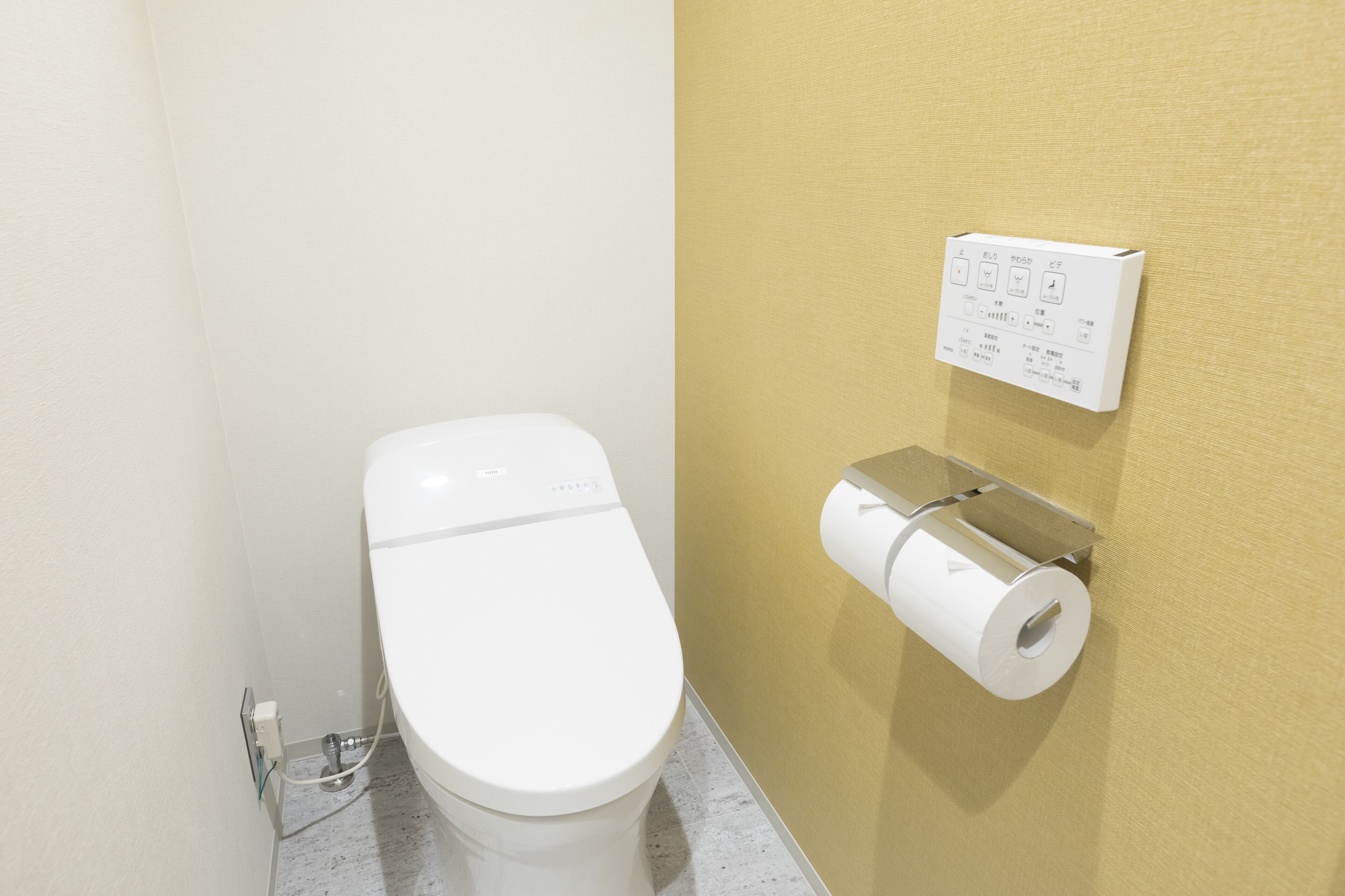 Inodoro con botón de descarga y dispensador de papel higiénico fijado a la pared.
