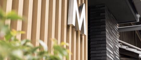 A building facade with vertical wooden slats and a large 'M' sign.