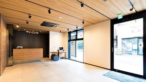 A modern reception area with a wooden reception desk, a 'Welcome' sign, and a large window offering a view of the street. - M’s Hotel Sanjo Omiya (Kyoto)
