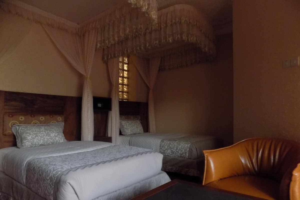 A hotel room with two beds, a leather armchair, and a canopy bed.