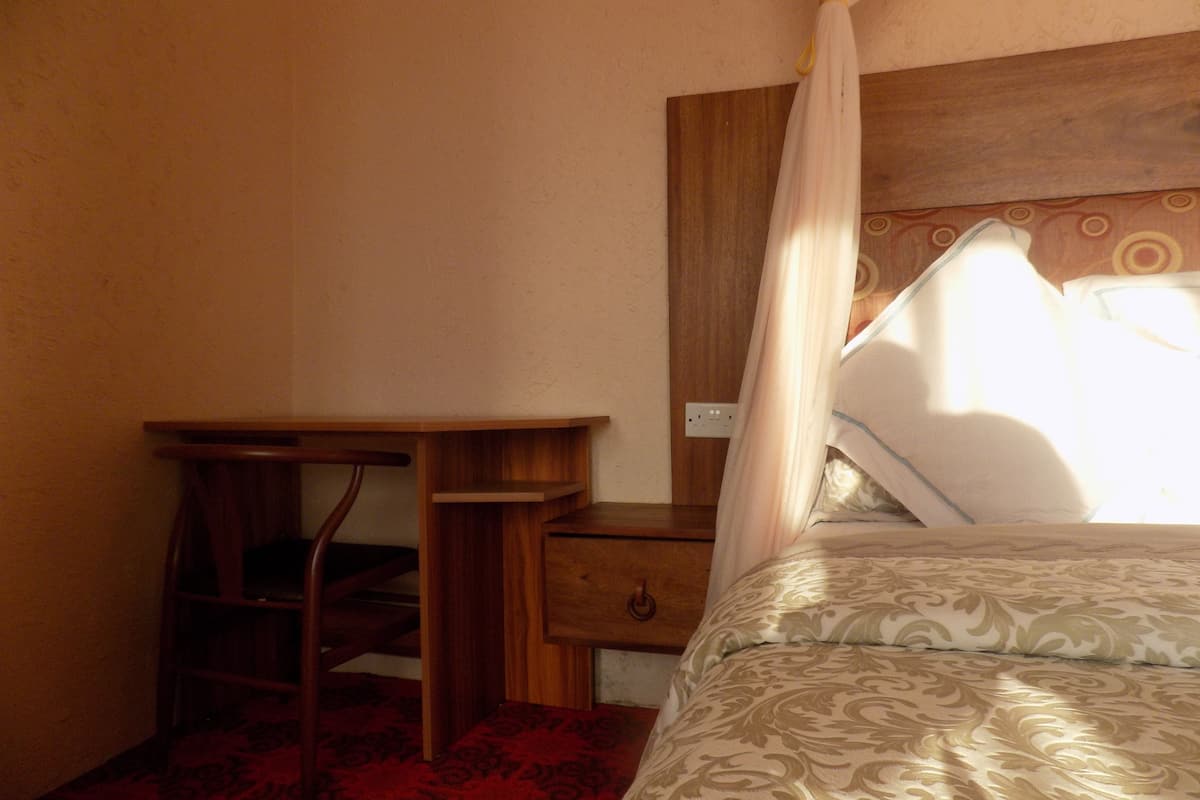 A bedroom with a bed, a wooden nightstand, a desk, and a chair.
