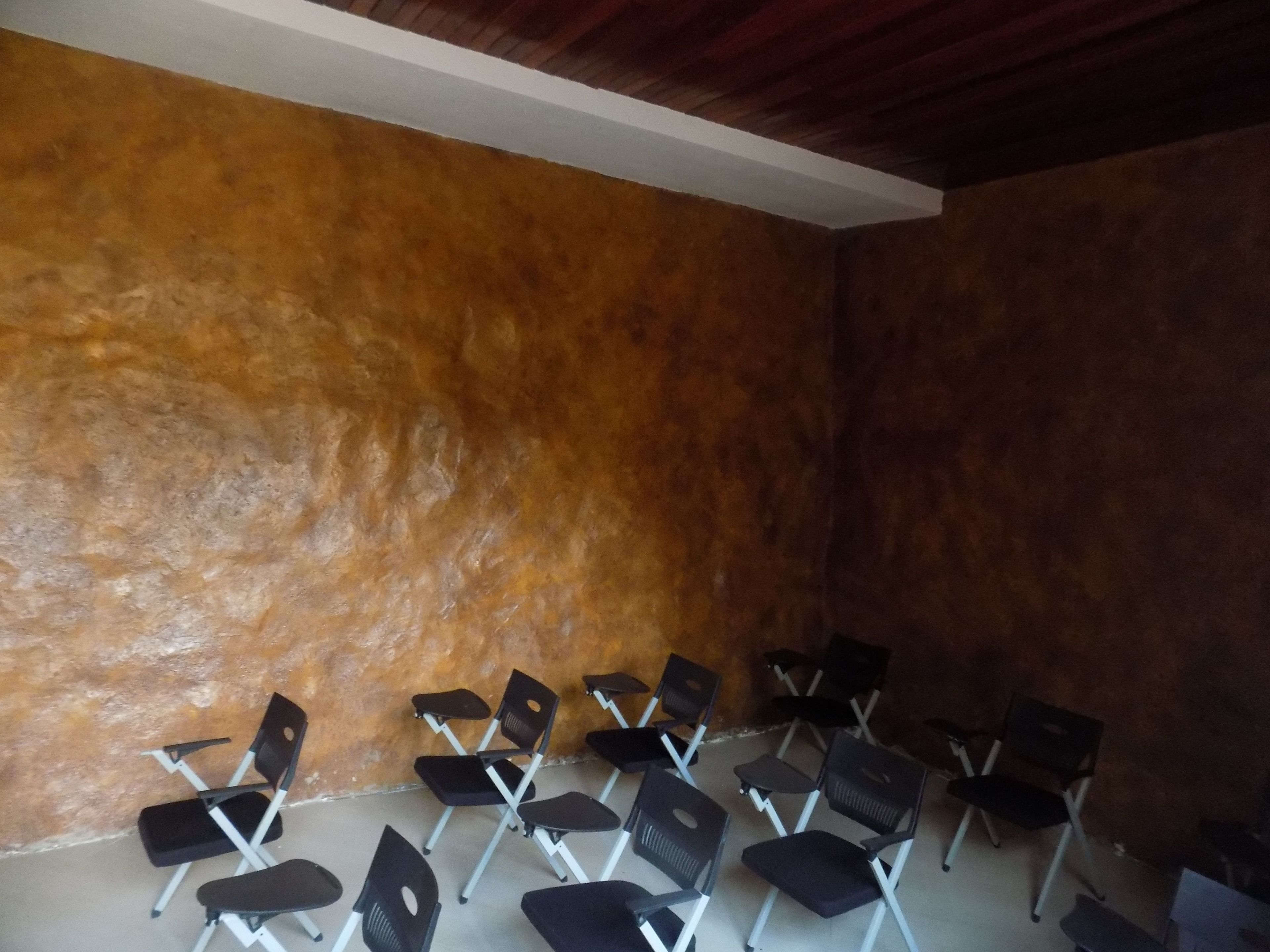 A room with a brown textured wall and a white ceiling. There are several black chairs arranged in rows.