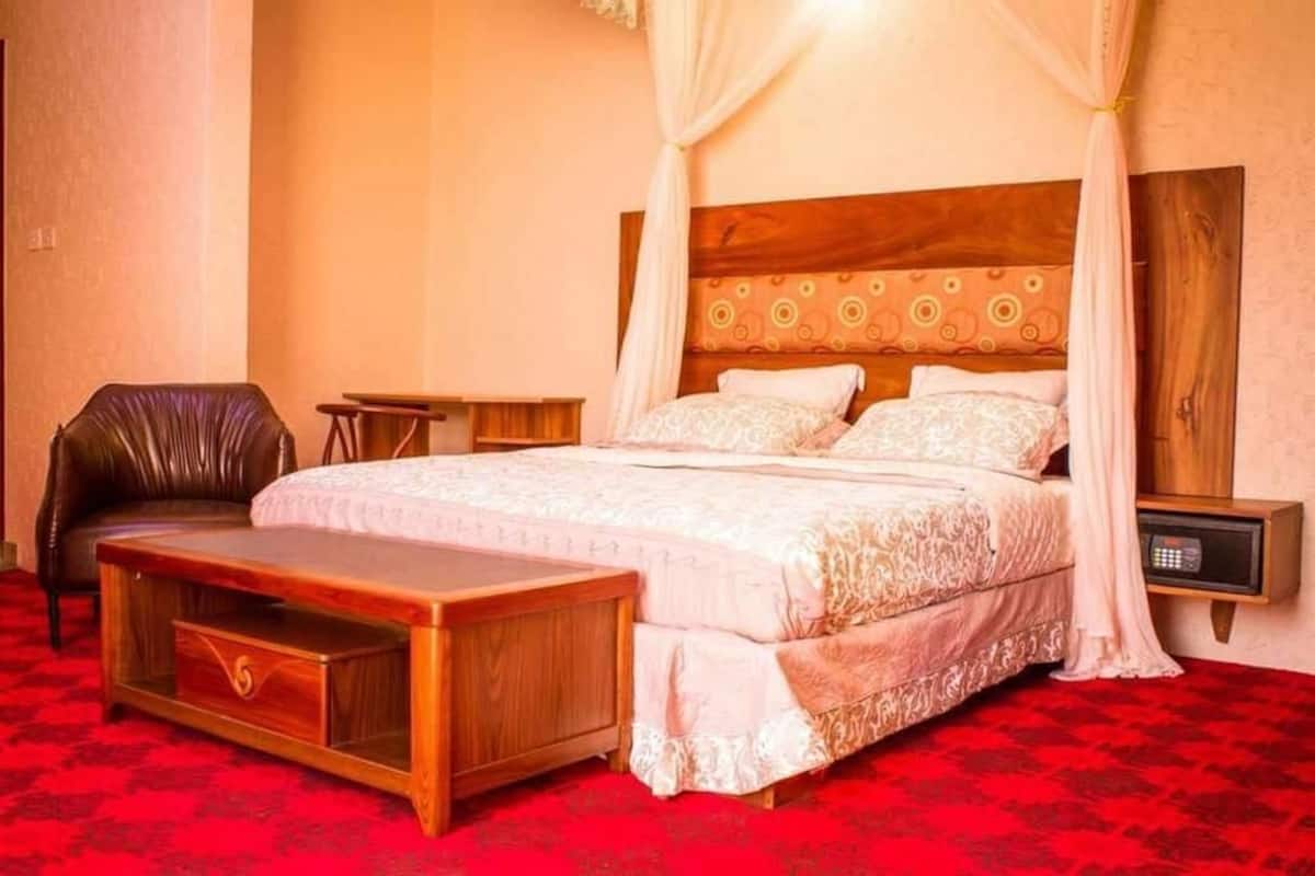 A bedroom with a large bed, a wooden nightstand, a leather chair, and a small table.
