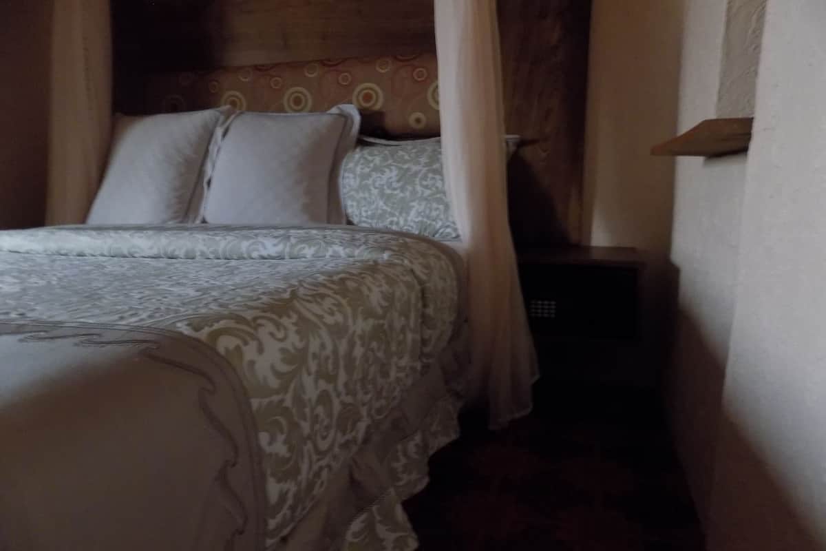 A bed with patterned bedding, a wooden headboard, and a nightstand with a lamp.