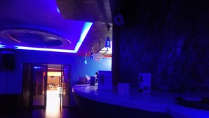 Ein schwach beleuchteter Raum mit gewölbter Decke, einer Bar mit Hockern und einer sichtbaren Tür zu einem weiteren Raum.