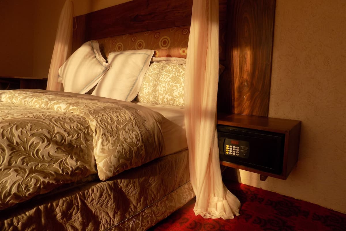 A bed with a canopy, a bedside table with a clock, and a patterned carpet.