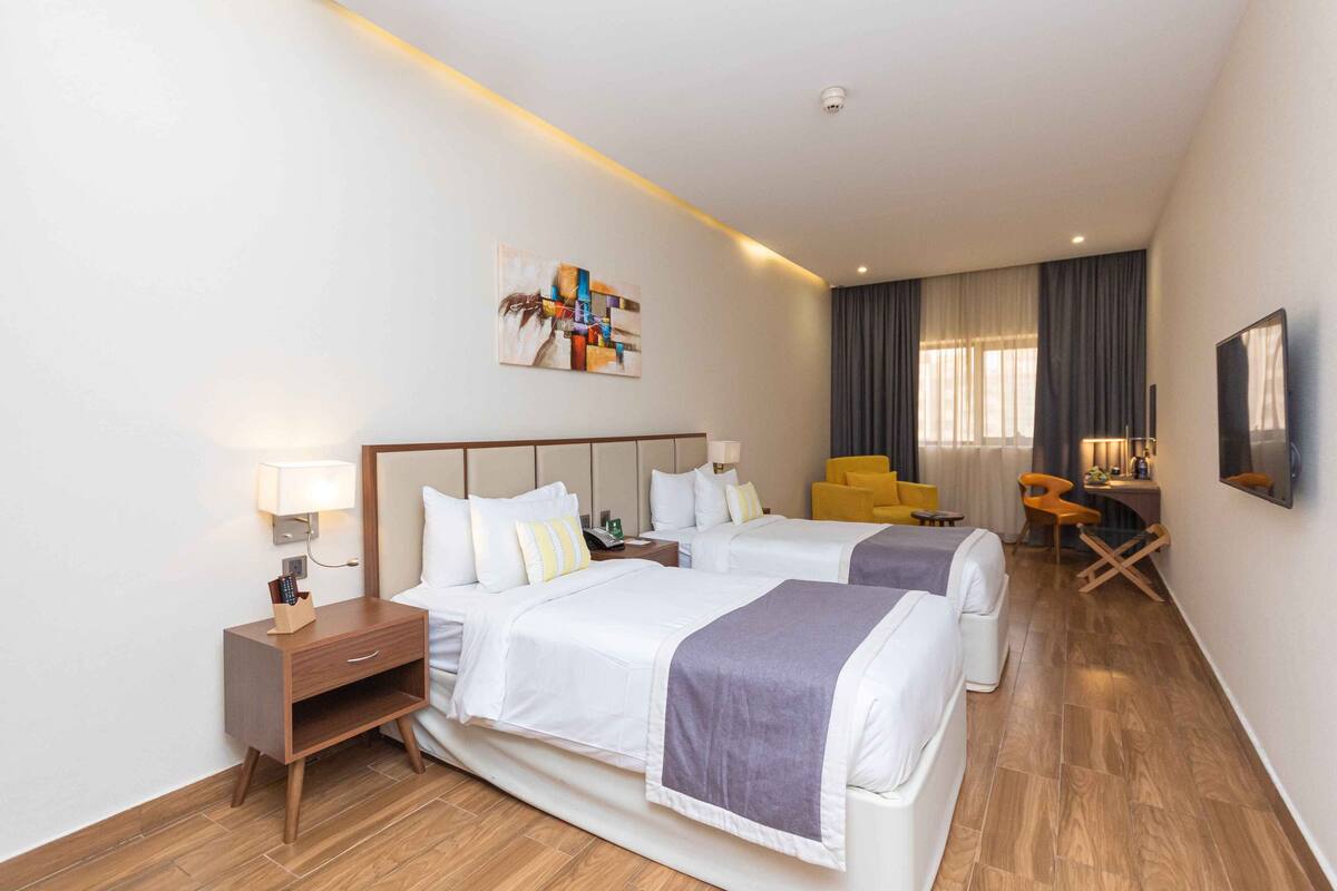 A hotel room with two beds, a desk, a chair, and a TV.