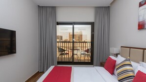 A hotel room with a large bed, a TV, a balcony with chairs, and a city view. - Le Wana Hotel (Dubai)