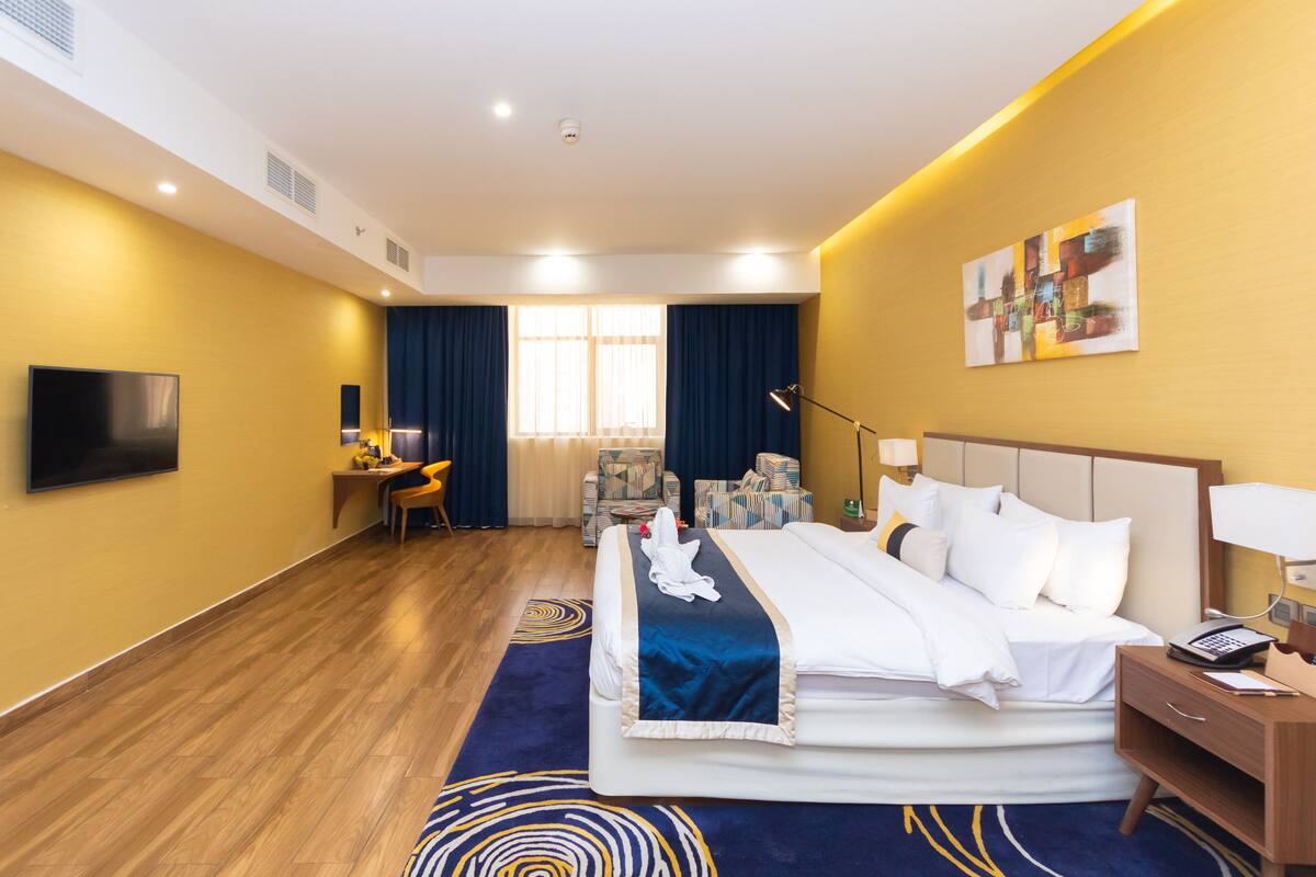 A hotel room with a bed, a desk, a chair, a TV, and a painting on the wall.