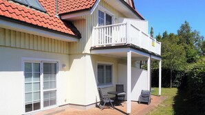 A two-story house with a balcony, a patio with outdoor furniture, and a red-tiled roof. - Centrally located apartment close to the beach for max. 4 pers. with terrace, WLAN, washing machine (Ostseebad Prerow)