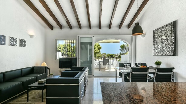 Un salon moderne comprenant un canapé, une table basse et un téléviseur, donnant sur un balcon aménagé avec des sièges d’extérieur.