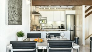 Une cuisine moderne dotée d’un îlot central, d’appareils électroménagers en acier inoxydable et d’un coin repas avec des chaises noires et une table blanche.