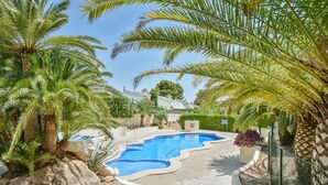 Une piscine entourée de palmiers et un bâtiment blanc avec un toit bleu.