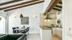 Une cuisine moderne avec des armoires blanches, un four à micro-ondes et un four encastré. On y trouve un coin repas avec une table et des chaises, et une suspension lumineuse est fixée au plafond.