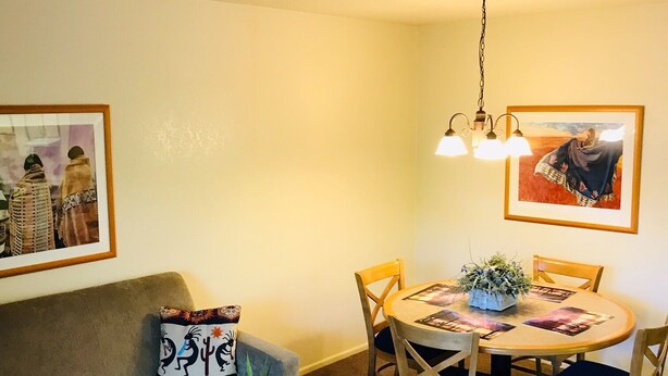 A cozy living room with a sofa, a coffee table with a plant, a dining table with chairs, and two wall-mounted light fixtures. - Cozy Condo in Chandler, entire unit to yourself with balcony in gated community. (Chandler)