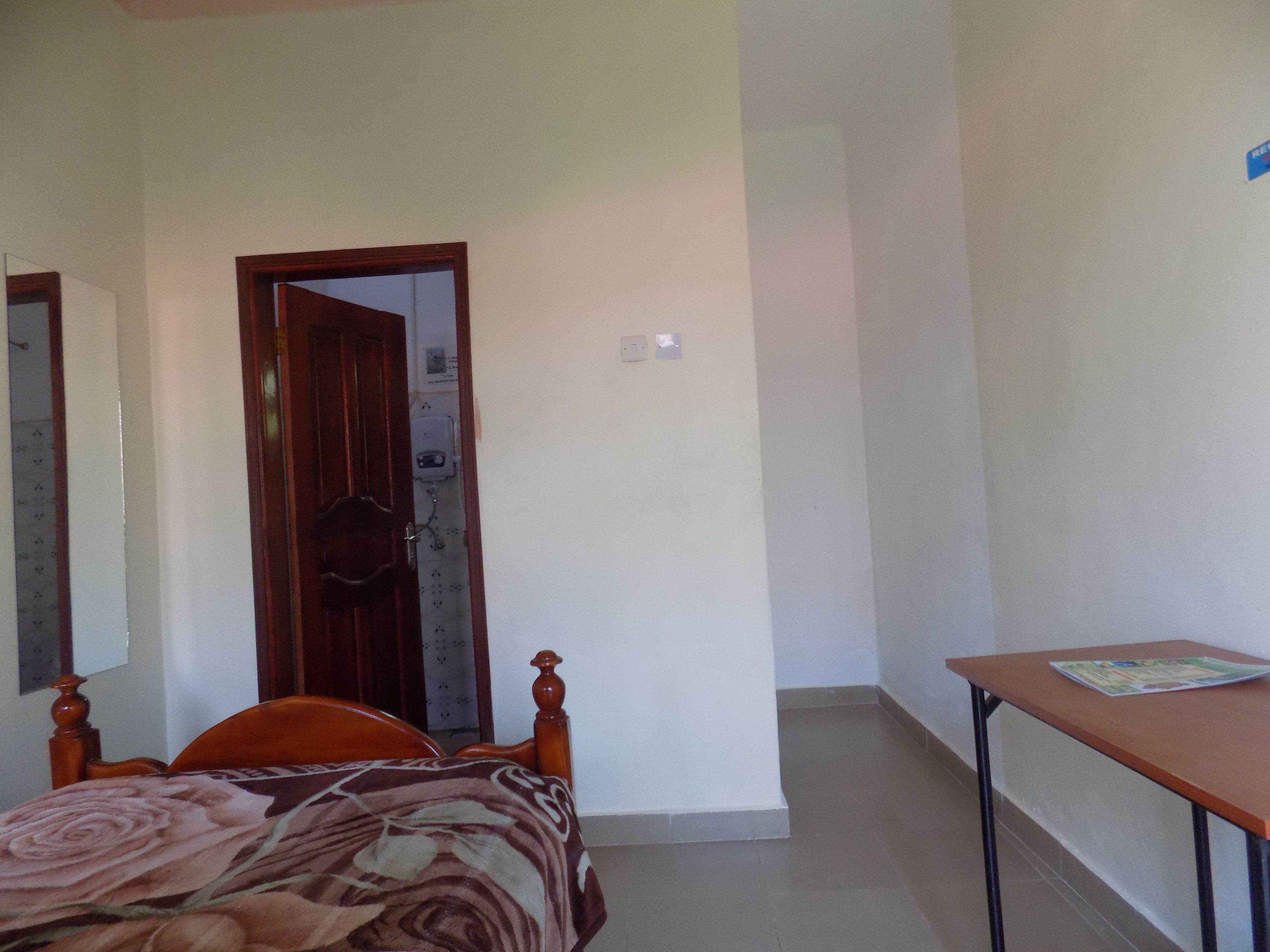 A bedroom with a wooden bed, a small table, and a door leading to another room.
