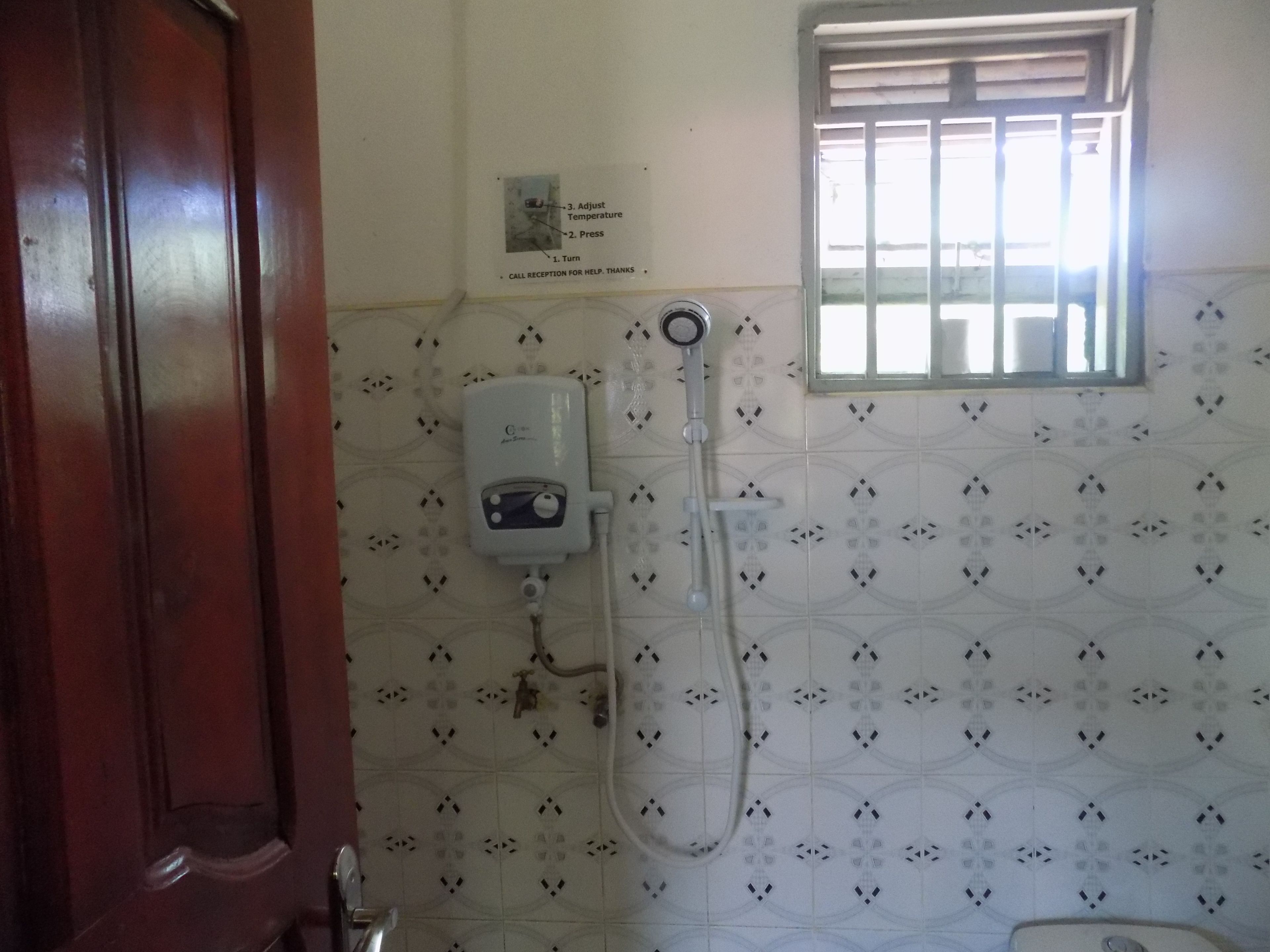 Un baño con ducha, un secamanos y una ventana con barrotes.