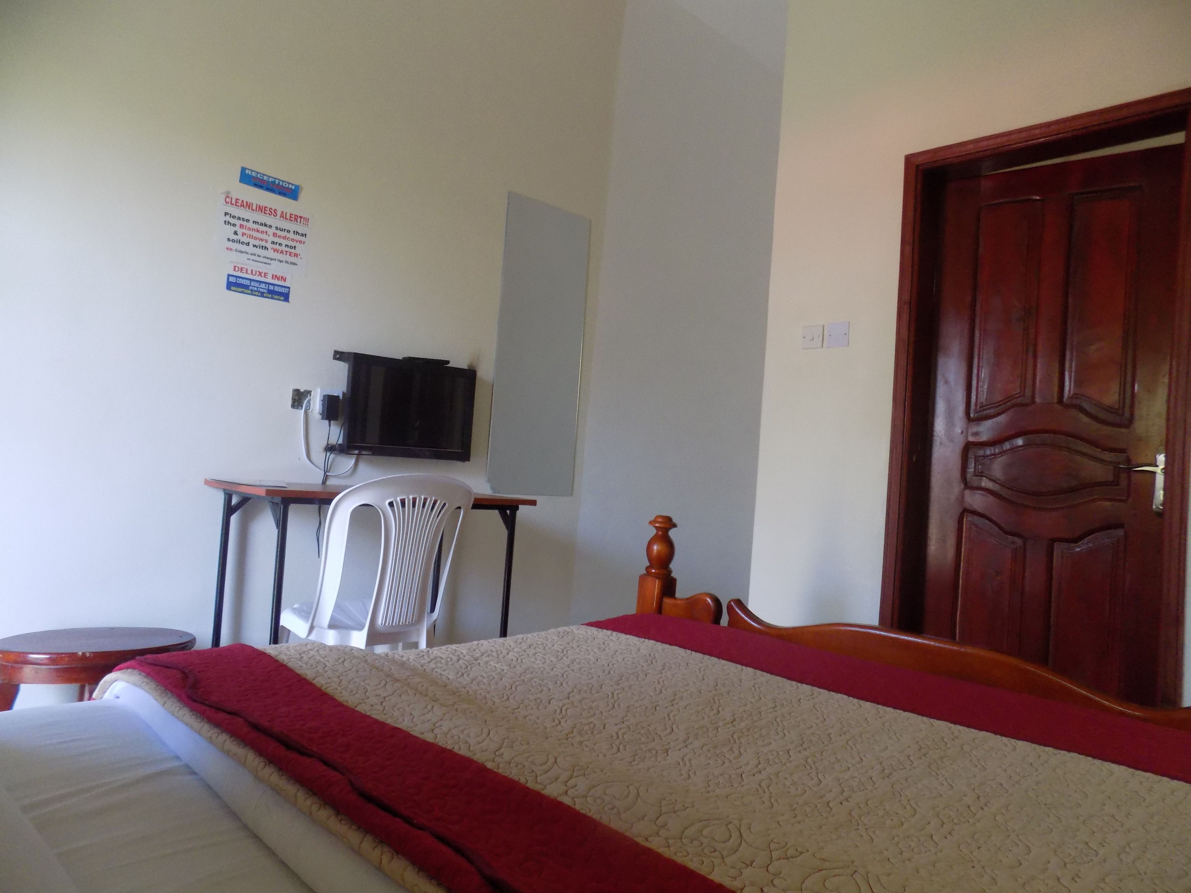 Een hotelkamer met een bed, een bureau met stoel, een televisie en een houten deur.