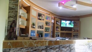 A bar area with shelves stocked with various bottles and a television mounted on the wall. - Deluxe Hotel - Ishaka (Ishaka)